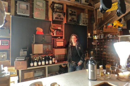 Angélica Castelló behind the bar and in front of a collection of old radios and navigation equipment.